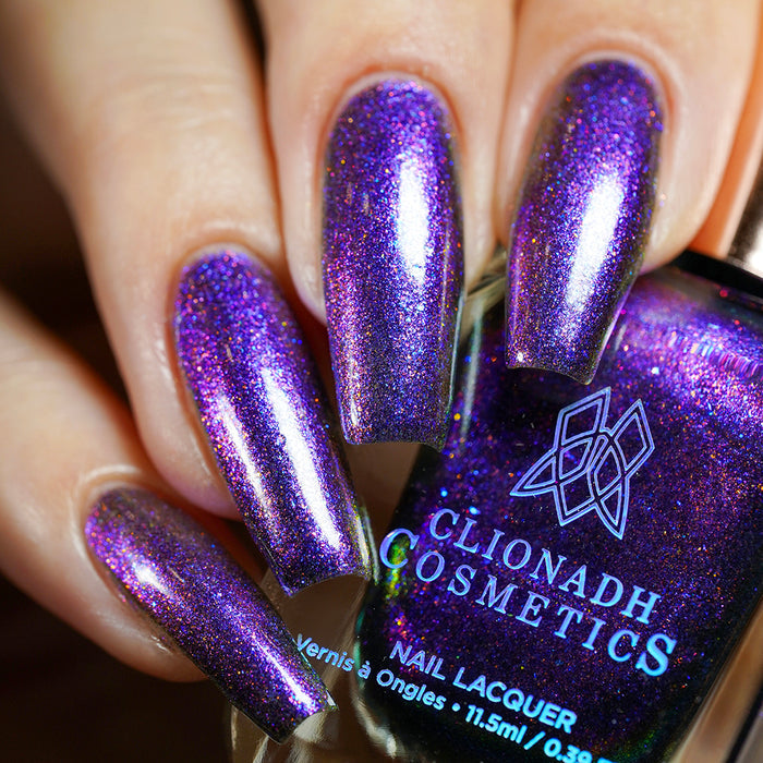 Close-up of nails painted with Liquidus Nail Lacquer on fair skin tone. Hand is holding polish bottle.
