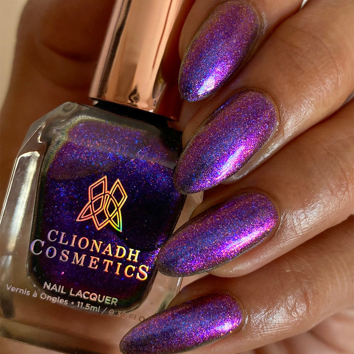 Close-up of nails painted with Liquidus Nail Lacquer on medium skin tone. Hand is holding polish bottle.