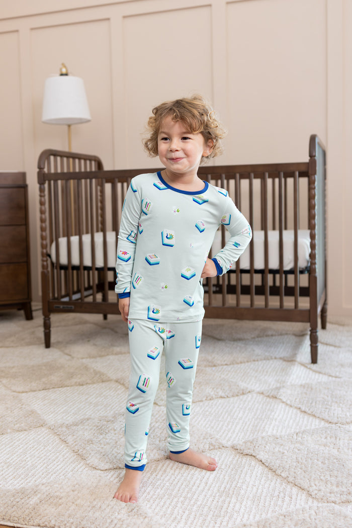Boy wearing Long Sleeve Pajamas in Dew Mahjong print posing in front of a crib