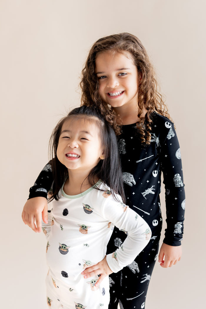 Two girls smiling wearing Long Sleeve Pajamas in in STAR WARS™ and Grogu™ print on a cream background