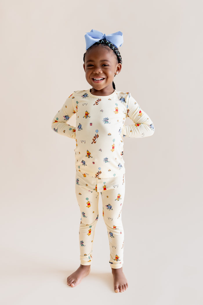 Girl posing in Long Sleeve Pajamas in Winnie the Pooh Celebration print on a beige background