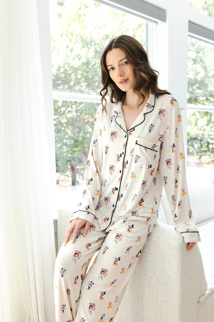 Model posing in Long-Sleeved Women's Pajama Set in Mickey Mouse & Friends print standing against a white sofa in living room