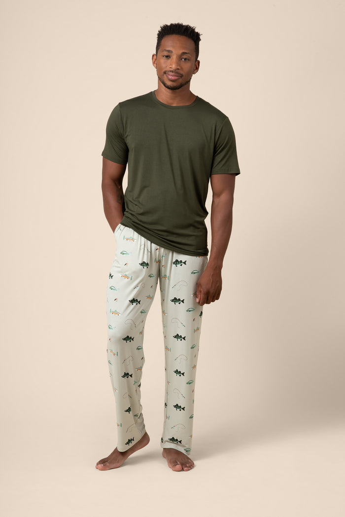 Man wearing a green t-shirt and fishing patterned pajama pants on a beige background