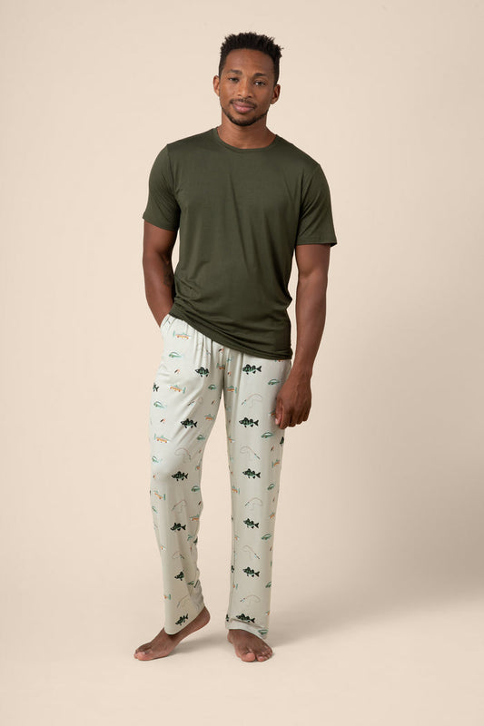 Man wearing a green t-shirt and fishing patterned pajama pants on a beige background