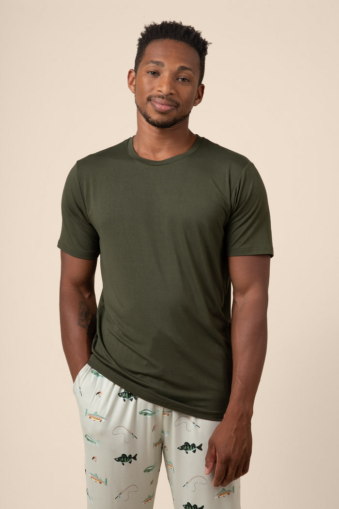 Man wearing an olive green t-shirt and light-colored pants with fish patterns on a beige background