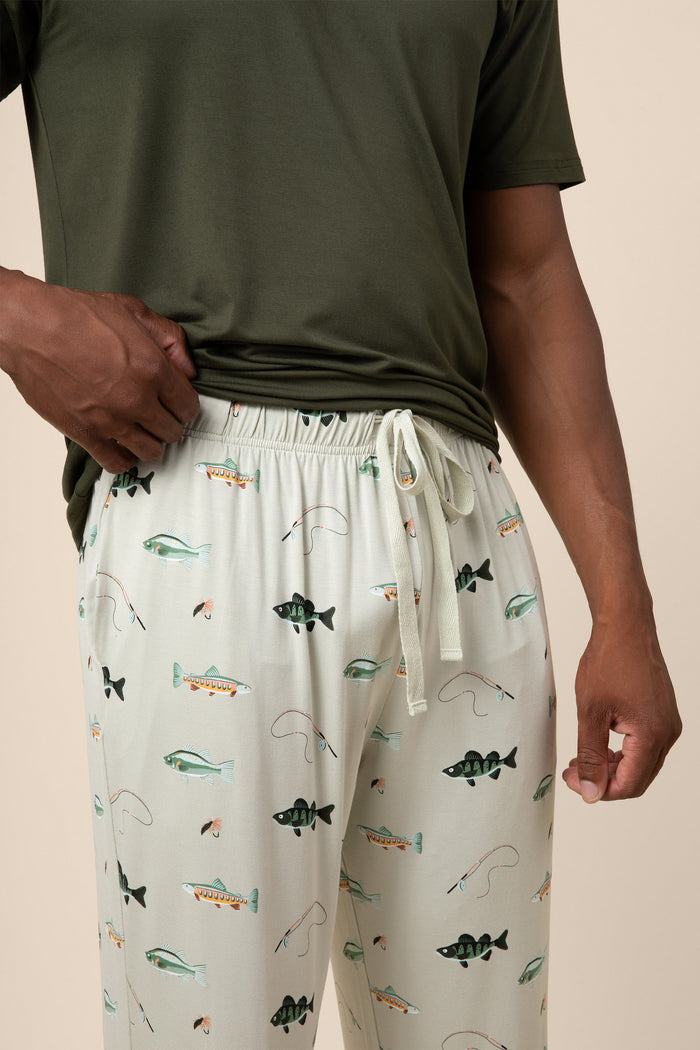 Person wearing a green t-shirt and fishing patterned pajama pants on a beige background