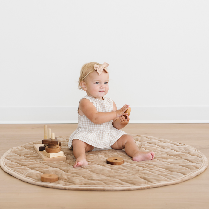 Baby girl sits on a hazelnut minky play mat  and is playing with some toys.