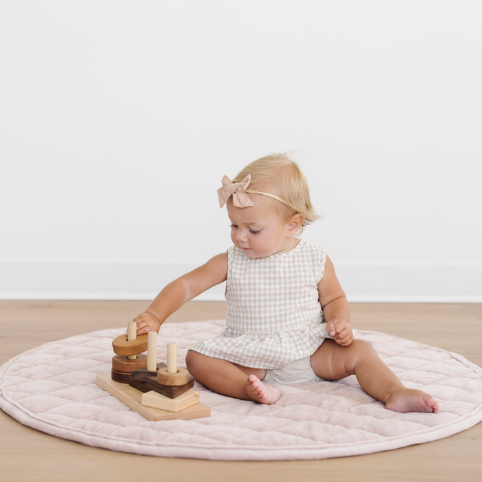 Baby girl sits on a pink minky play mat with some toys.