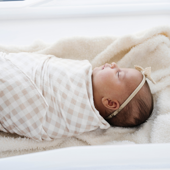 Newborn baby girl swaddles in gingham minky stretch luxe swaddle baby blanket.