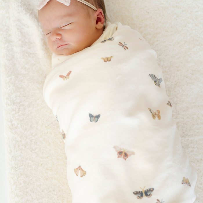 A newborn baby girl is swaddled in a minky stretch luxe blanket that has butterflies on it.