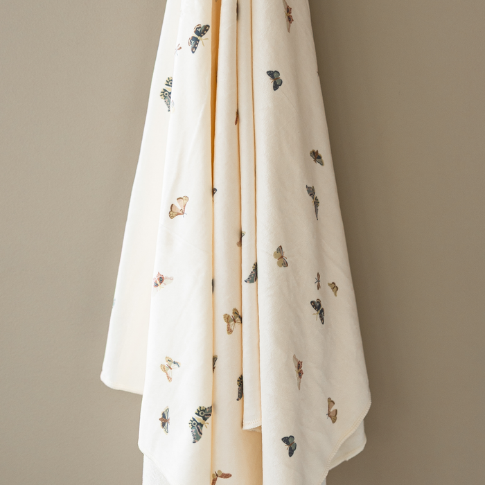 A butterfly minky stretch luxe swaddle that is hanging in front of a taupe background.