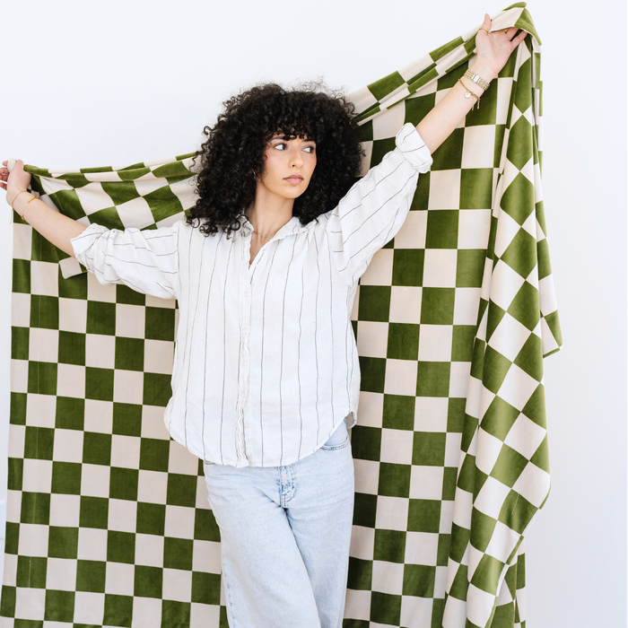 Woman stands with a Minky Stretch olive checkered throw blanket stretched out behind her.