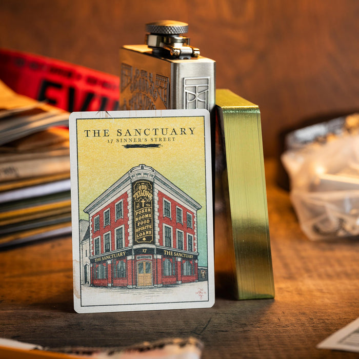 Metallic flask with a card featuring 'The Sanctuary' building on a wooden surface.