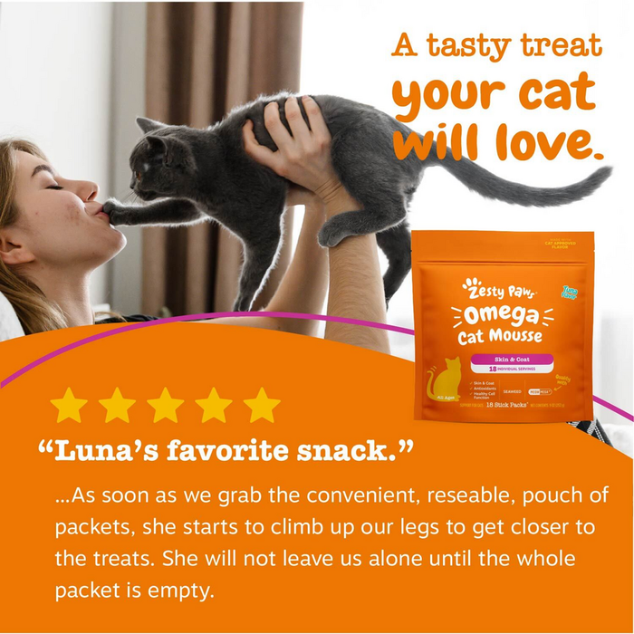 Gray cat being held up toward a woman's face next to orange Omega Cat Mousse treat pouch.