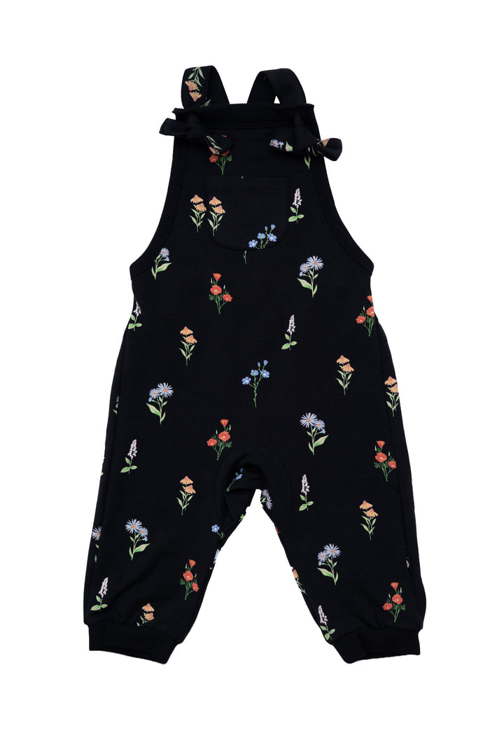 Black baby overall jumpsuit with an all-over colorful wildflower print, featuring adjustable shoulder ties and elastic cuffed ankles, shown on a plain white background.