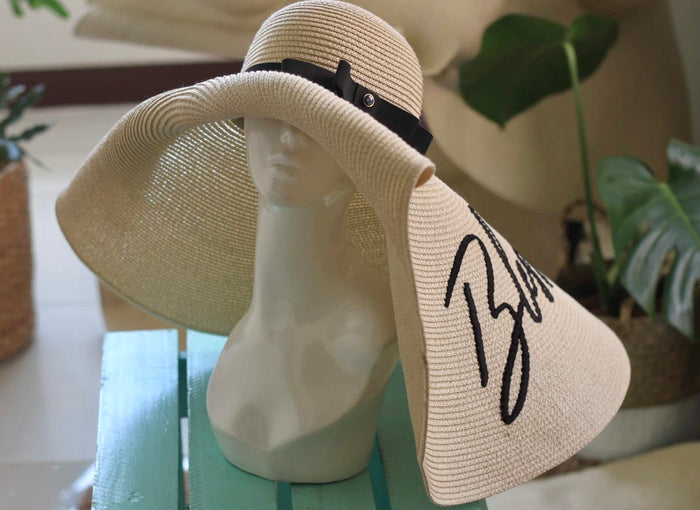 Oversized straw sun hat with wide brim and black ribbon detail displayed on mannequin head