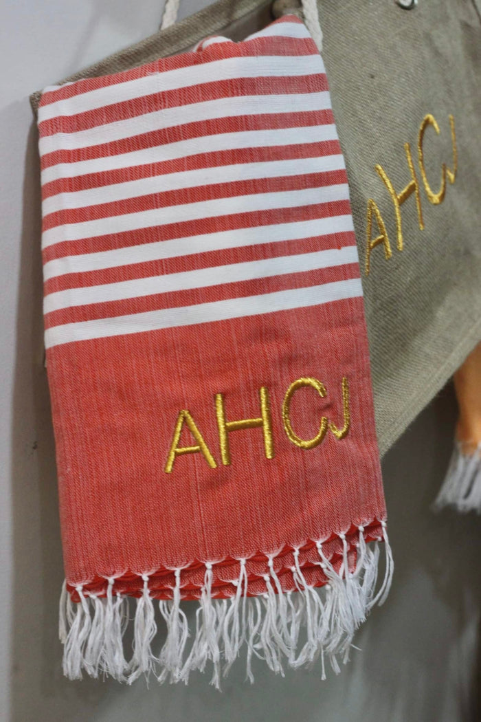 Personalized beach towel in red and white stripes with yellow embroidered initials and fringed edges