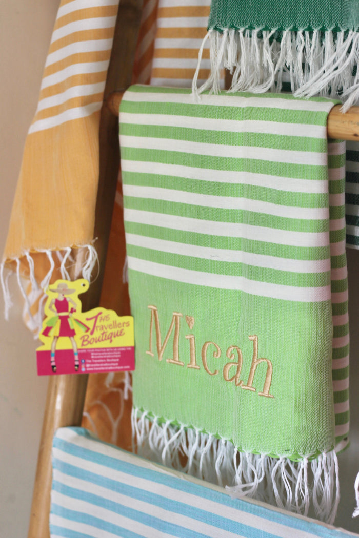Green and white striped personalized beach towel with fringed edges and the name Micah embroidered