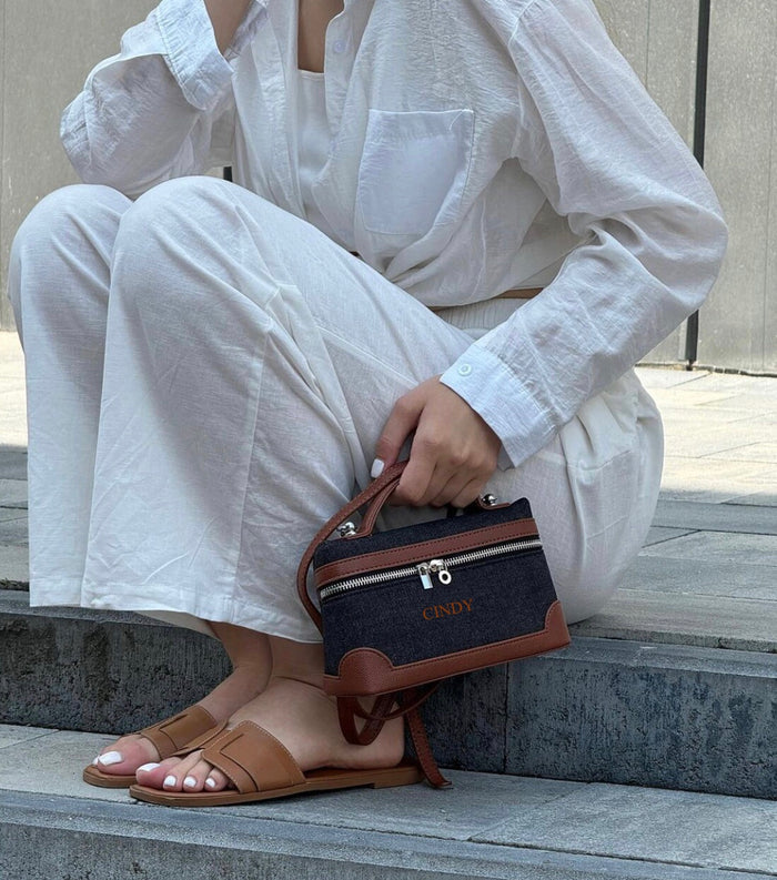 Custom square denim purse with brown leather accents held by woman wearing white outfit and brown sandals