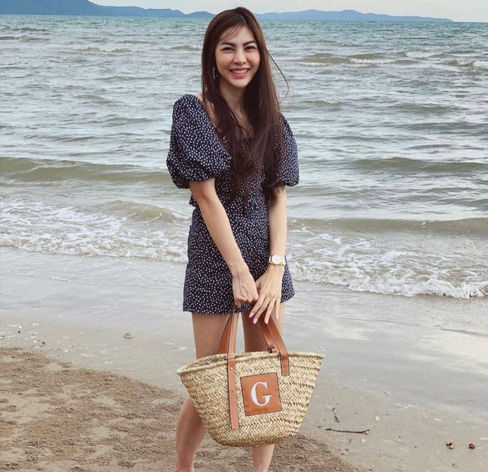 Woman holding seagrass basket handbag with leather handles on the beach by the ocean waves