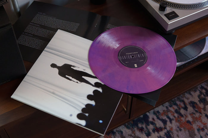 A translucent purple Acceptance album vinyl sits partially on its cover, which features the silhouette of a person walking with shadows and blurred figures. An open lyric sheet and a turntable are nearby.
