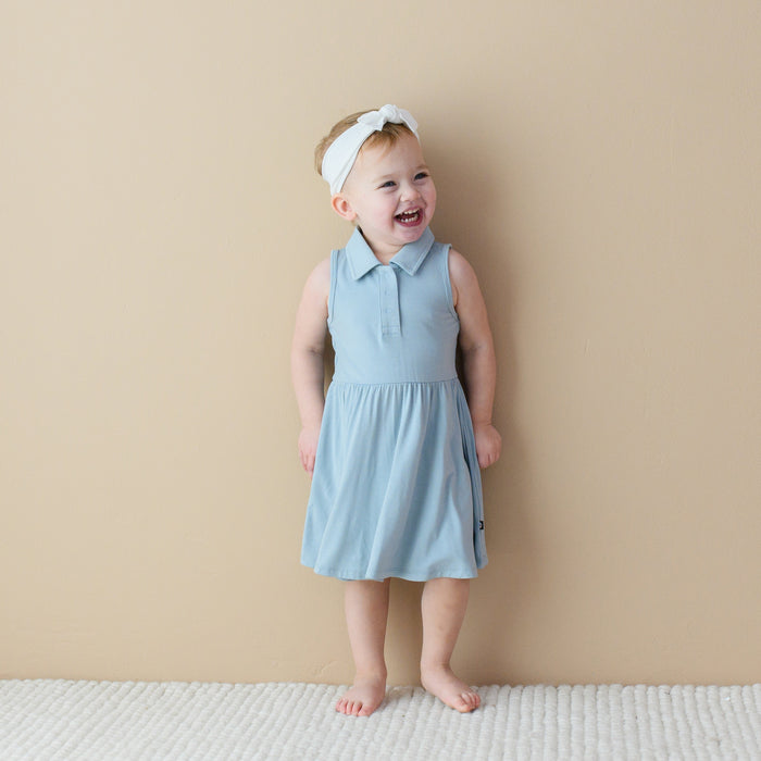 Toddler standing in-front of a tan wall while wearing a  Polo Bodysuit Dress in Fog