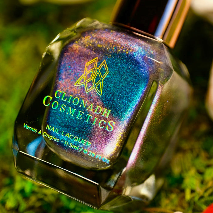 Angled, close-up of Psilocin Nail Lacquer bottle, on a blurred grass background.