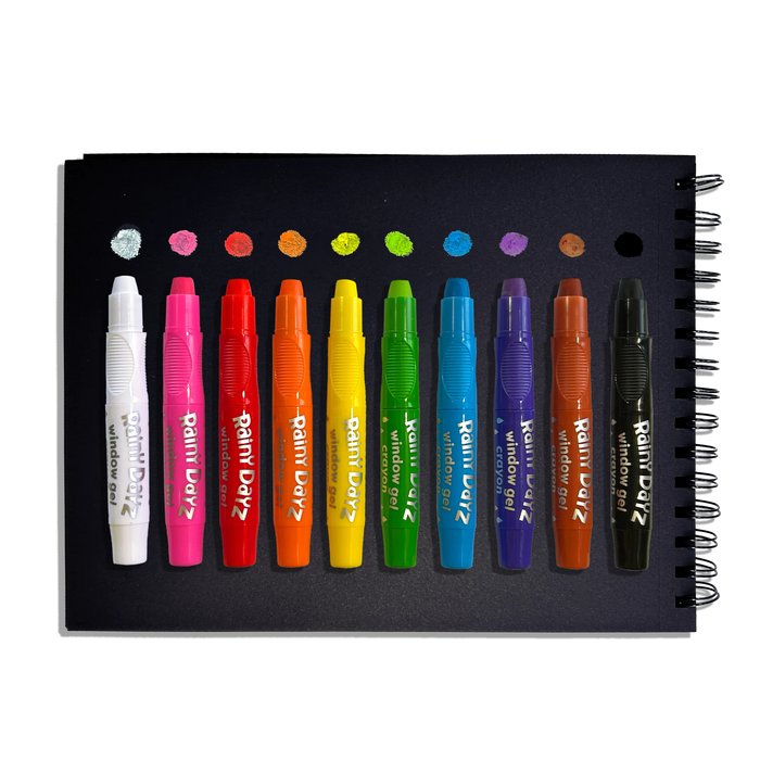 Row of uncapped OOLY Rainy Dayz Window Gel Crayons on a black paper sketchbook with swatches on a white background