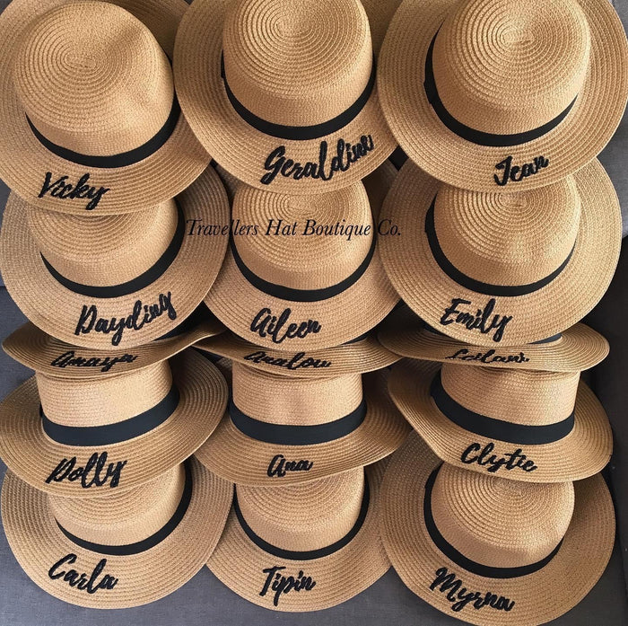 Custom embroidered round hat collection from Travellers Hat Boutique featuring names on tan straw hats with black bands