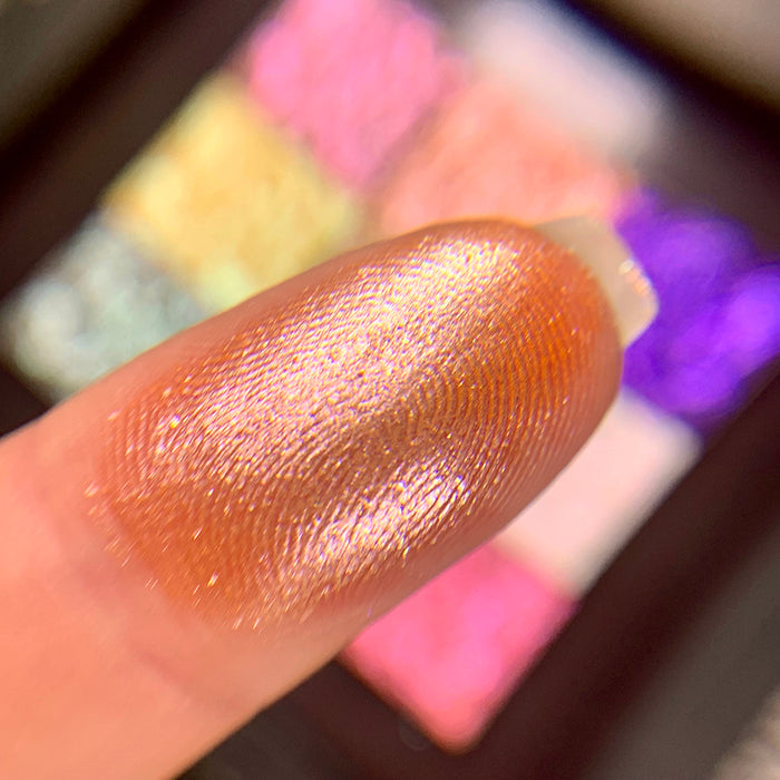 Close-up finger swatch of the eyeshadow Scroll on fair skin tone. Blurred palette in the background.