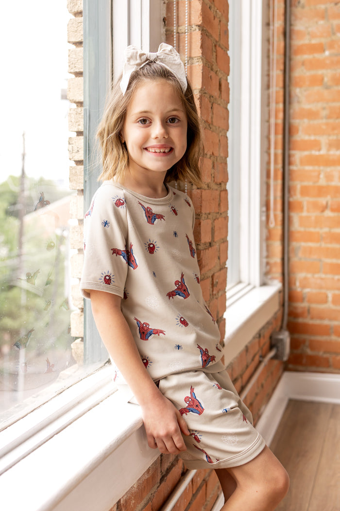 Girl posing in front of a window wearing an oat color Short Sleeve Jogger Set with Spider-Man print and oat color bow on head