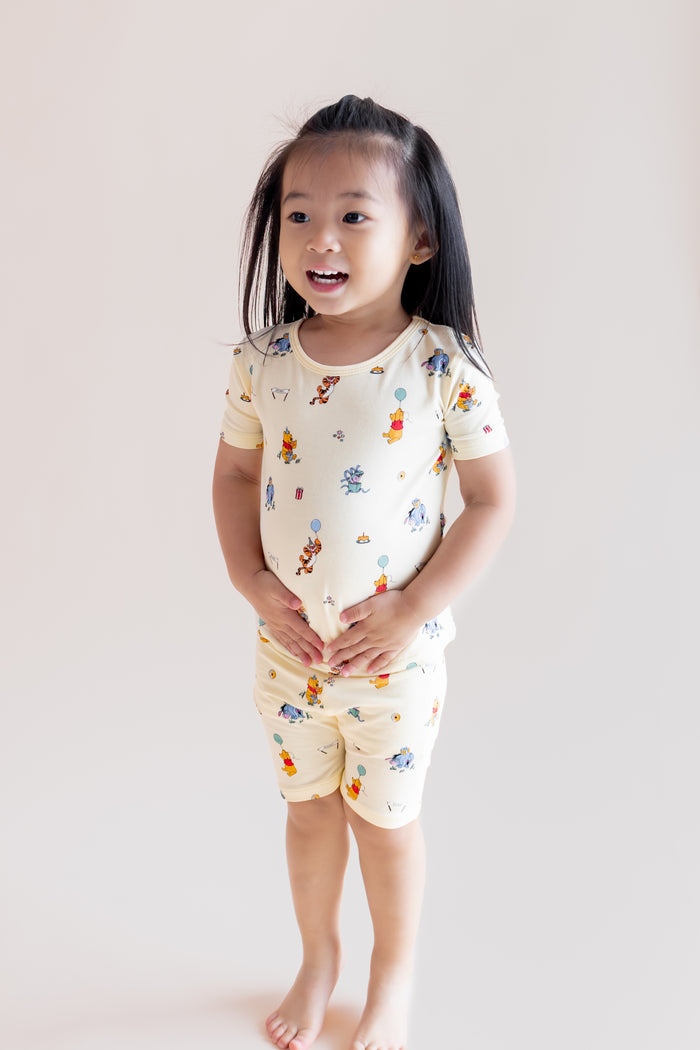 Girl posing wearing a Short Sleeve Pajamas in Winnie the Pooh Celebration print on a cream background