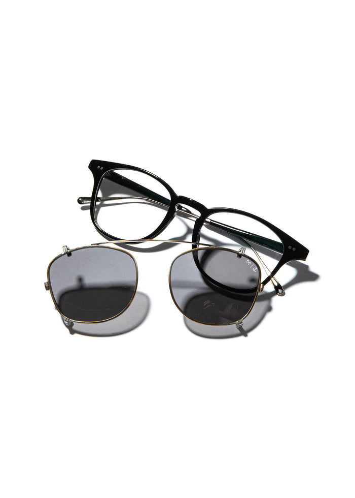 Black eyeglasses with detachable round clip-on sunglasses, casting shadows on a white background.