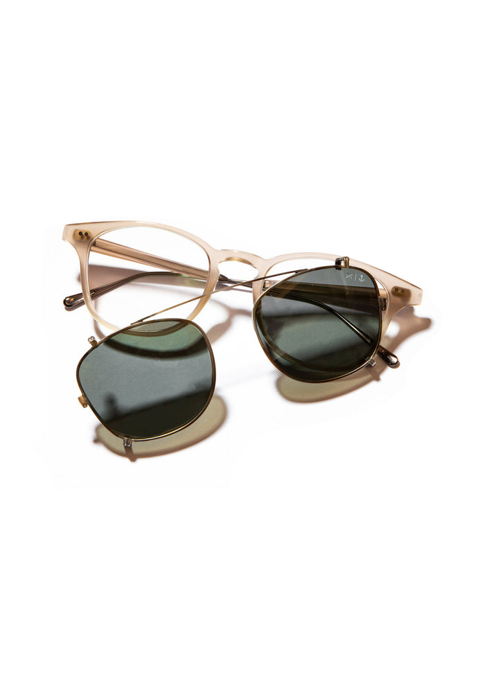 Clear eyeglasses with detachable green-tinted clip-on sunglasses, set against a white background, showcasing versatility.