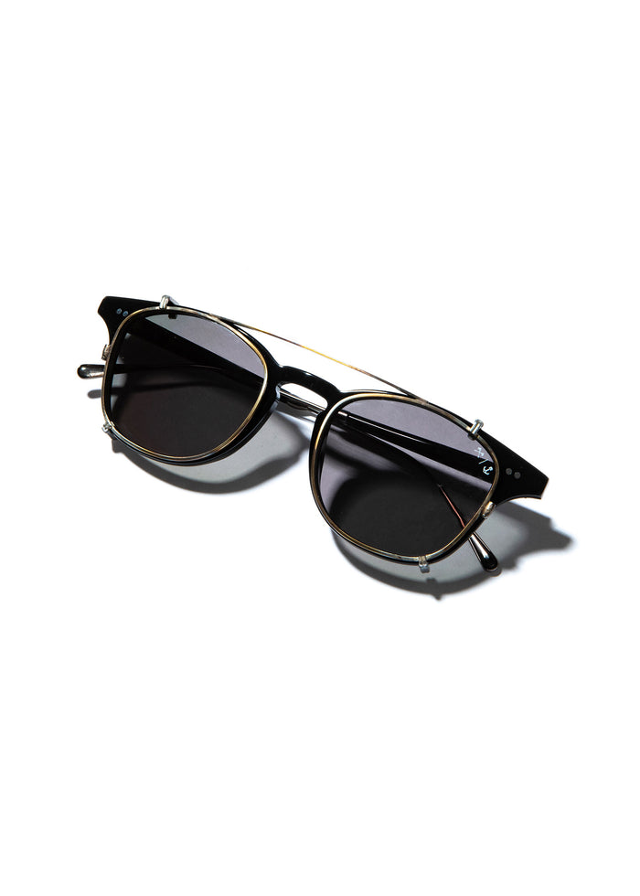 Stylish black sunglasses with gold accents on a white background, casting a shadow.