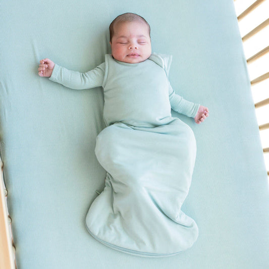 Infant sleeping in a crib and wearing a  Sleep Bag in Sage 2.5 with a long sleeve Sage romper underneath