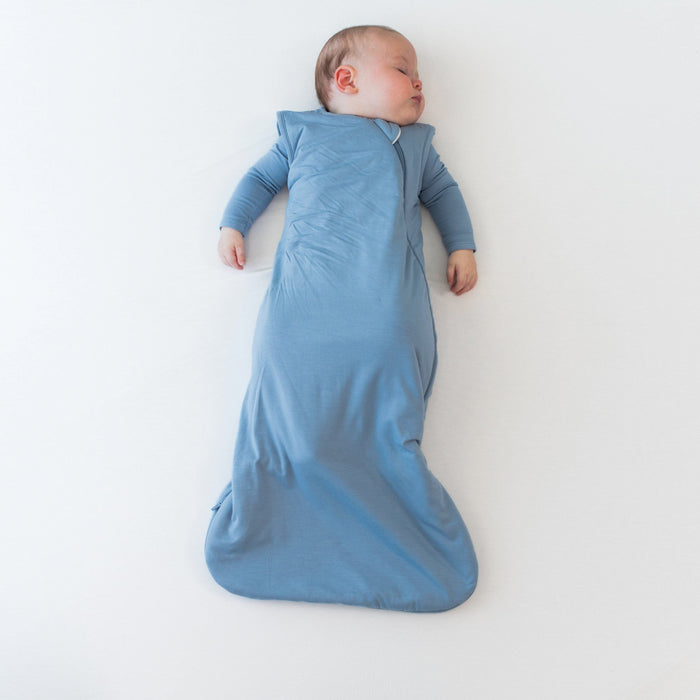 Baby sleeping on a flat off-white surface in the 2.5 Sleep Bag in Slate
