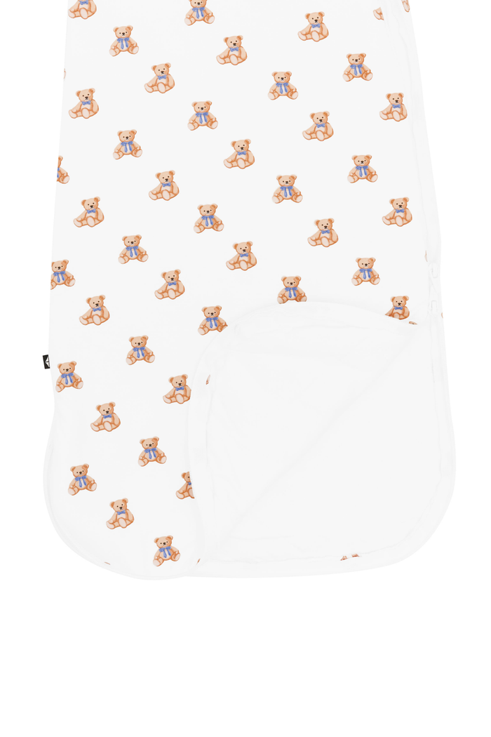 A white baby swaddle blanket featuring a repeating pattern of small teddy bears wearing blue outfits, with a solid white reverse side.