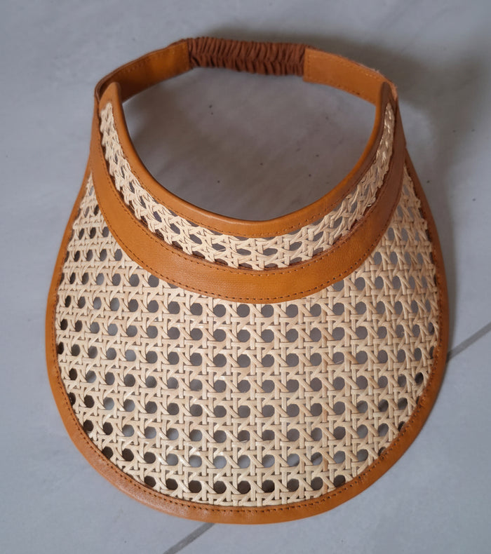 Woven visor with brown leather trim on a gray background