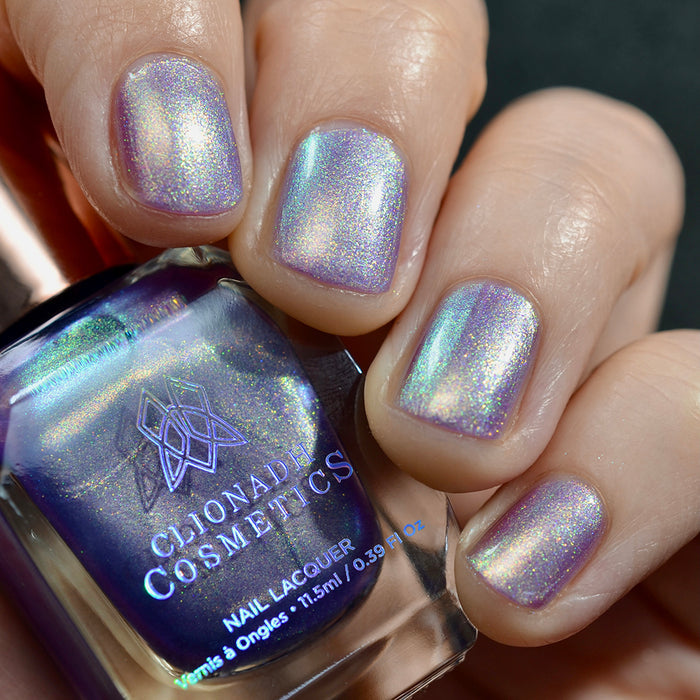 Close-up of nails painted with Royalty Nail Lacquer on fair skin tone. Hand is holding polish bottle.