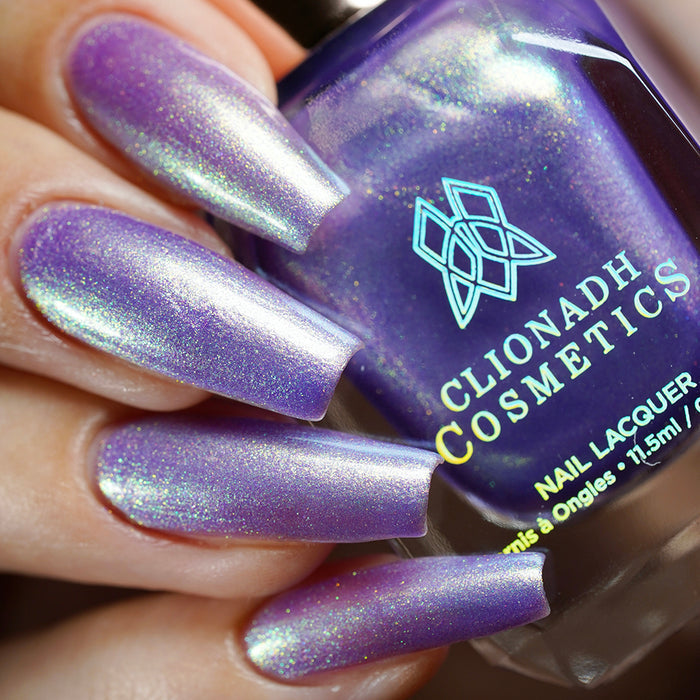 Close-up of nails painted with Royalty Nail Lacquer on fair skin tone. Hand is holding polish bottle.
