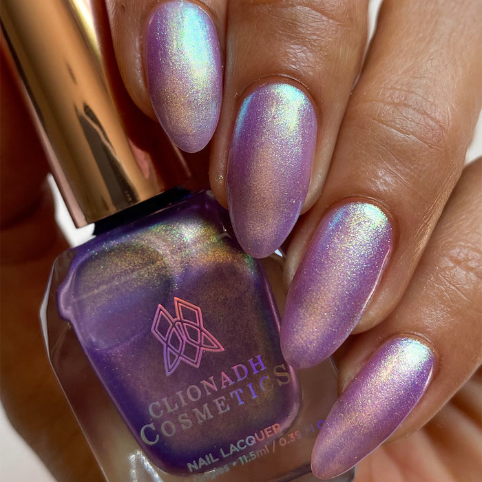Close-up of nails painted with Royalty Nail Lacquer on medium skin tone. Hand is holding polish bottle.
