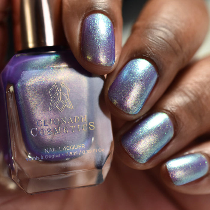Close-up of nails painted with Royalty Nail Lacquer on deep skin tone. Hand is holding polish bottle.