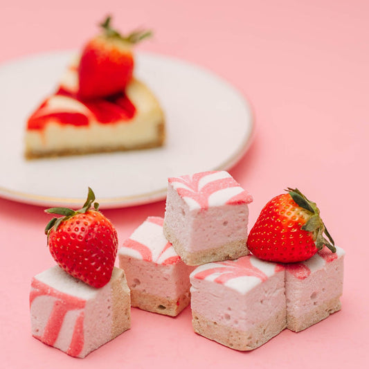 XO Marshmallow Gourmet Strawberry Cheesecake marshmallows with strawberries on them and a plate of cheesecake in the background