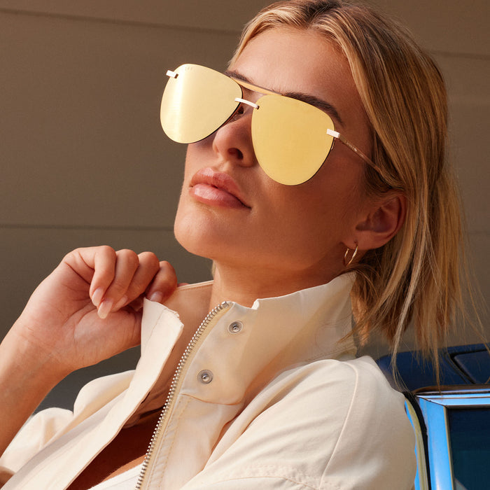 lifestyle - blonde female lounging in the sun wearing Tahoe sunglasses with brushed gold frames and gold mirror lens front view