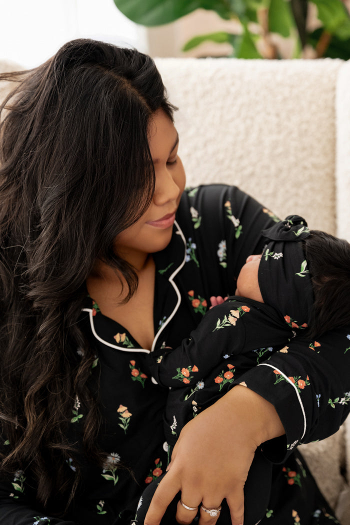 Model wearing Long sleeve women's pajama set in midnight wildflower print holding a baby wearing take me home set with bow in similar print