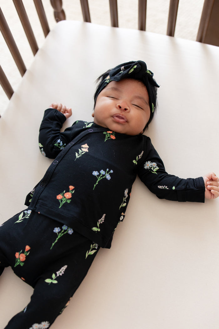 Baby sleeping in crib wearing Take Me Home Set with Bow in Midnight Wildflower print lying on a beige crib sheet.