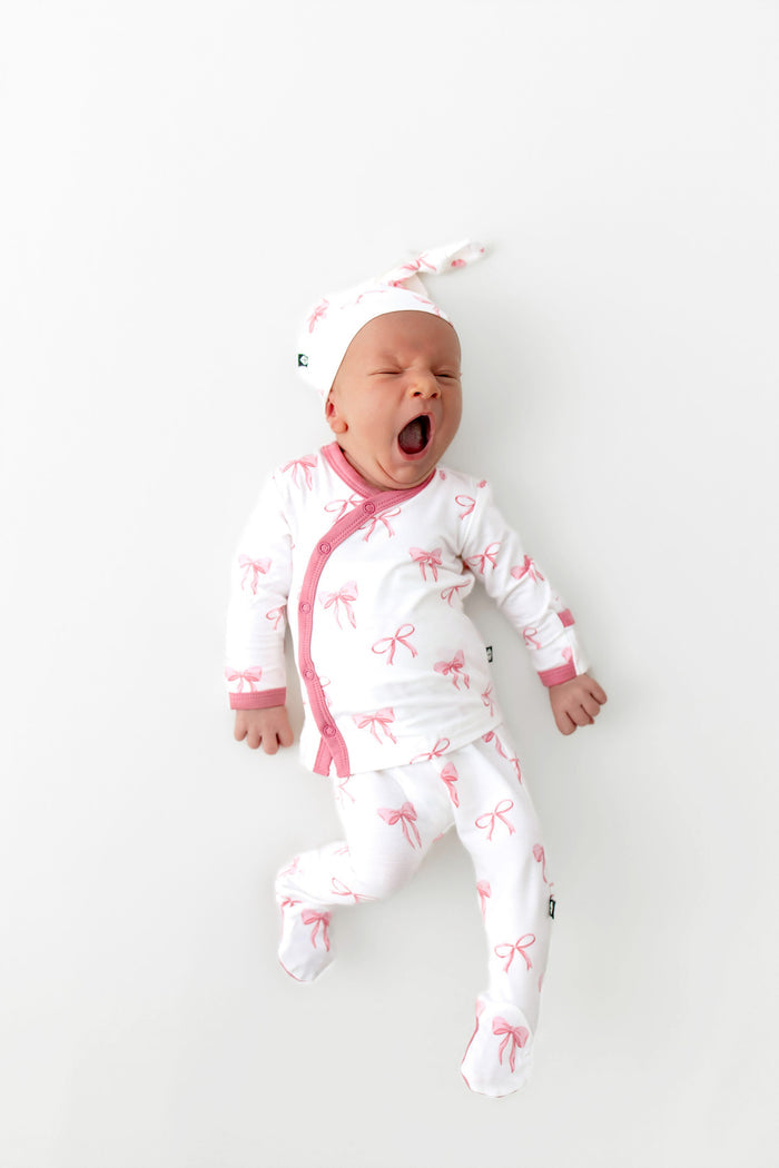 Baby in a pink and white onesie with bow pattern on a white background