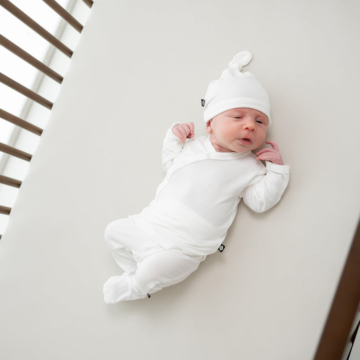 Baby in a wooden crib wearing a take me home set in a white color
