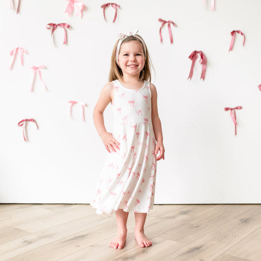 Child modeling Tank Twirl Dress in Bow with a bow background